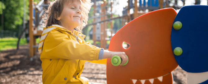 A young boy practicing ways to attain emotional intelligence by swinging on a playground dinosaur