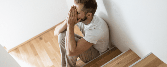 a man sitting on the stairs with his head in his hands, upset about something | Depression vs sadness